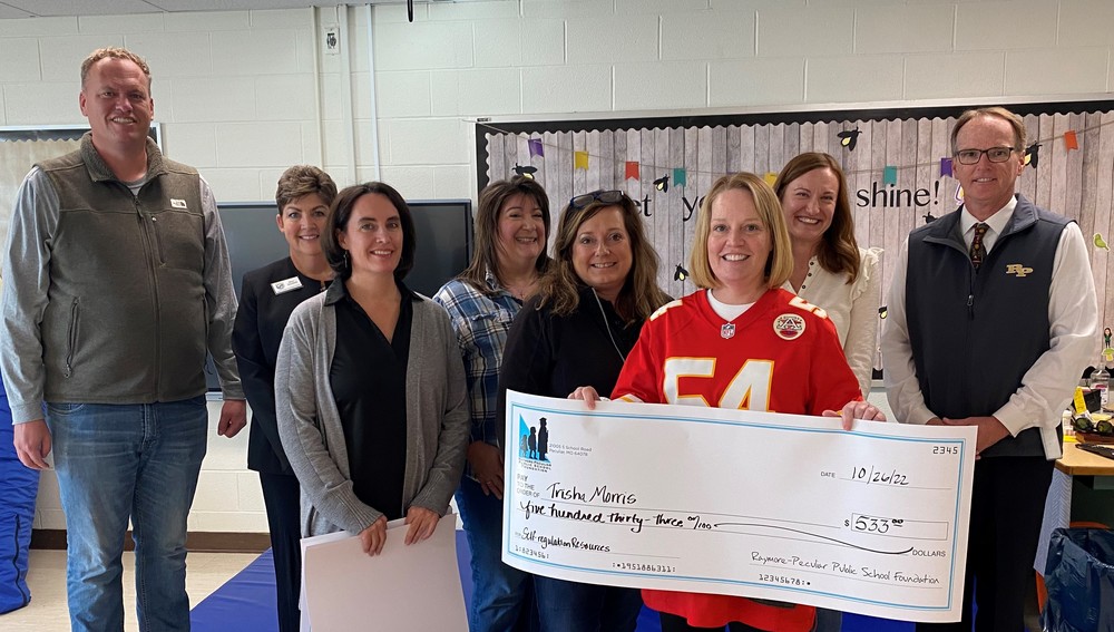 Teacher holding large check with foundation members.