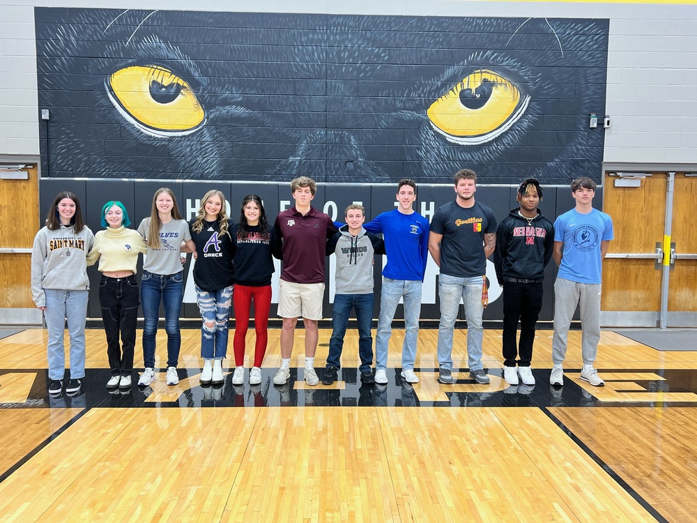 Eleven student athletes stand in front of the Panther Mural