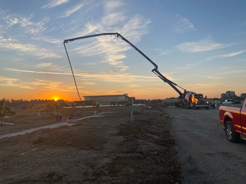 Workers pour concrete at construction site with sunrise in background